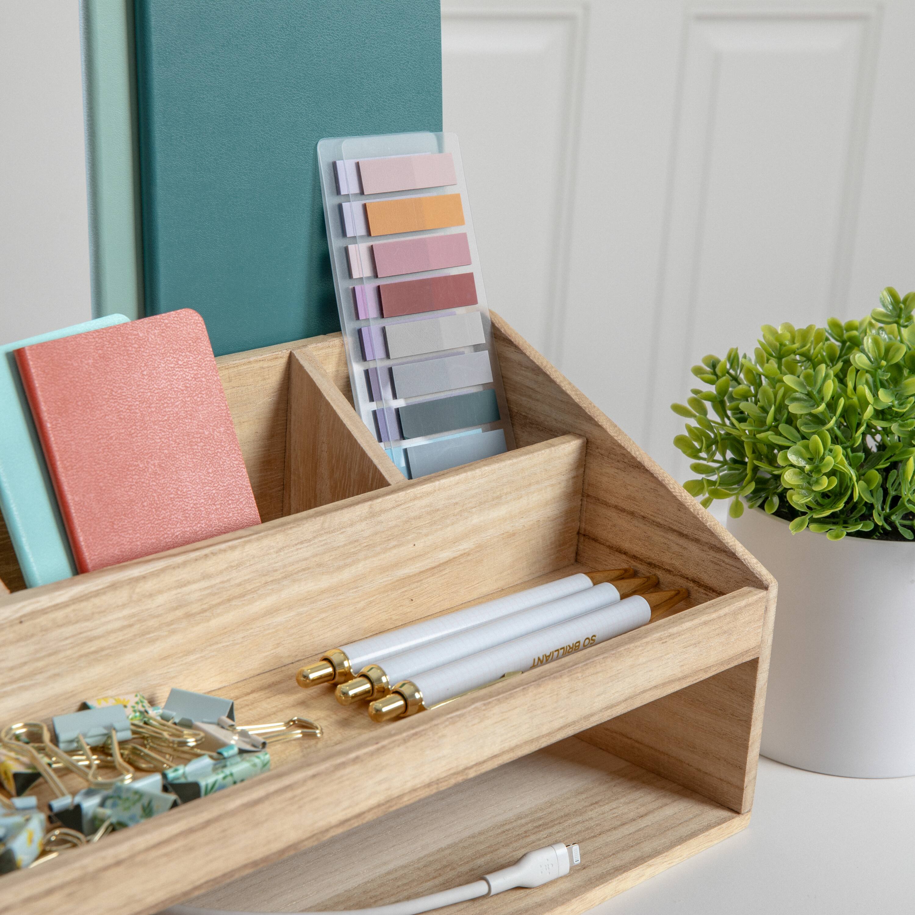 The text "28 OF IN SOTERILLIA LEA BRCCIA" is not related to the image. It appears to be an unrelated piece of text. The image features a wooden tray with various items, including a pencil pouch, a notebook, a plant, and a color palette.