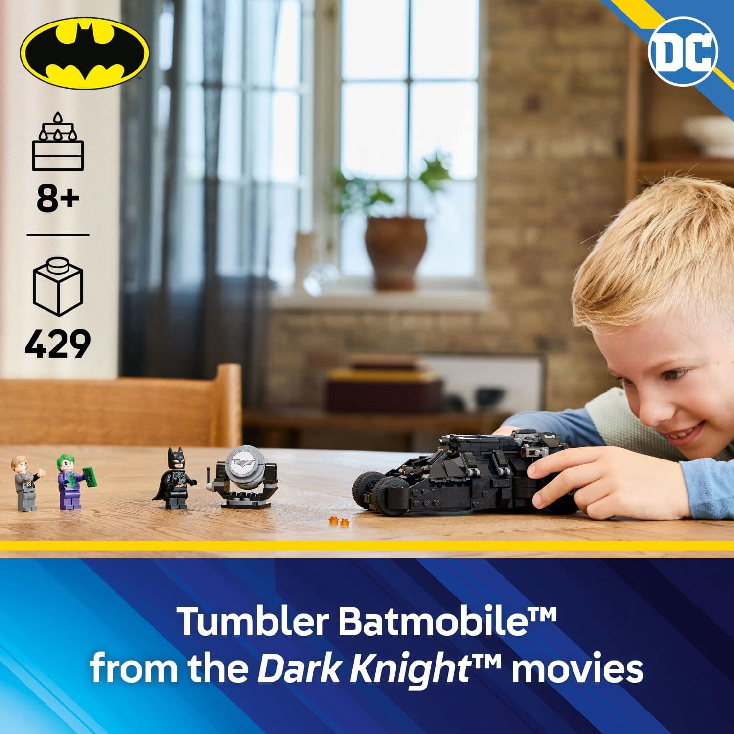 The image features a young boy playing with a toy Batmobile, which is a part of the Tumbler Batmobile set from the Dark Knight movies. The boy is sitting at a dining table, surrounded by various items such as a potted plant, a vase, and a bowl. The scene captures the excitement and fun of playing with toys, especially when they are inspired by popular movies like the Dark Knight series.