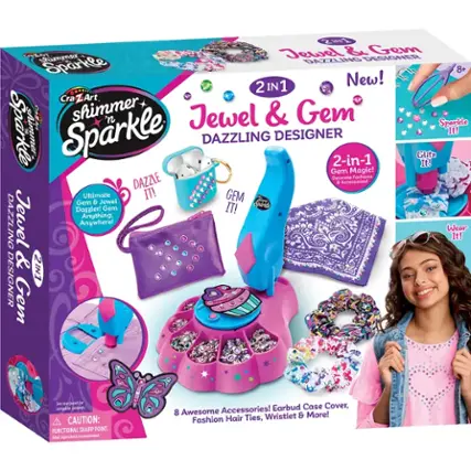 The image features a box of Shimmer 'n Sparkle Jewel & Gem Dazzling Designer, which includes a 2-in-1 jewelry and gem set. The box contains a variety of accessories, such as hair ties, a wristlet, and an earbud case cover. The box also comes with a warning that the product has a functional sharp point, and adult supervision is recommended. The image showcases a young girl holding the box, excited to use the new jewelry and gem set.