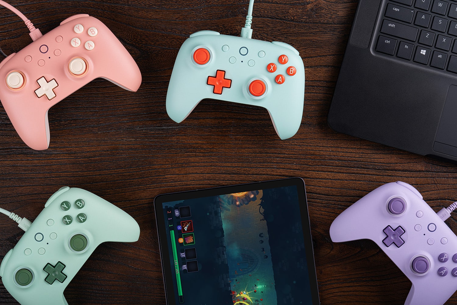 The image shows a table with five different colored Wii remotes and a tablet. The tablet is placed in the center of the table, surrounded by the remotes. The remotes are of various colors, including pink, blue, green, and purple. The tablet is likely used for playing games or controlling the remotes.