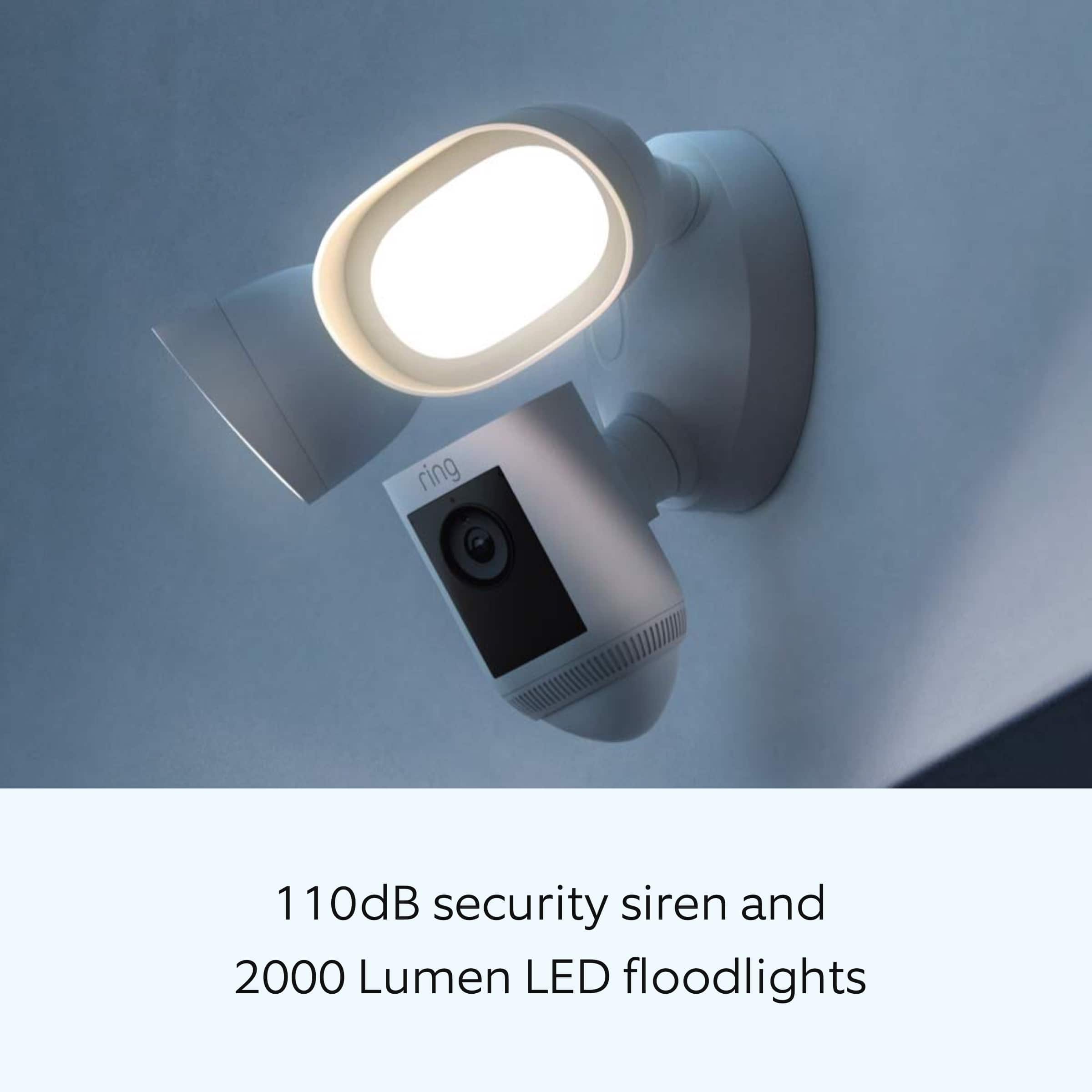 The image features a white light fixture with a security camera attached to it. The light fixture is designed to emit a 110 dB security siren and has 2000 Lumen LED floodlights to provide illumination.