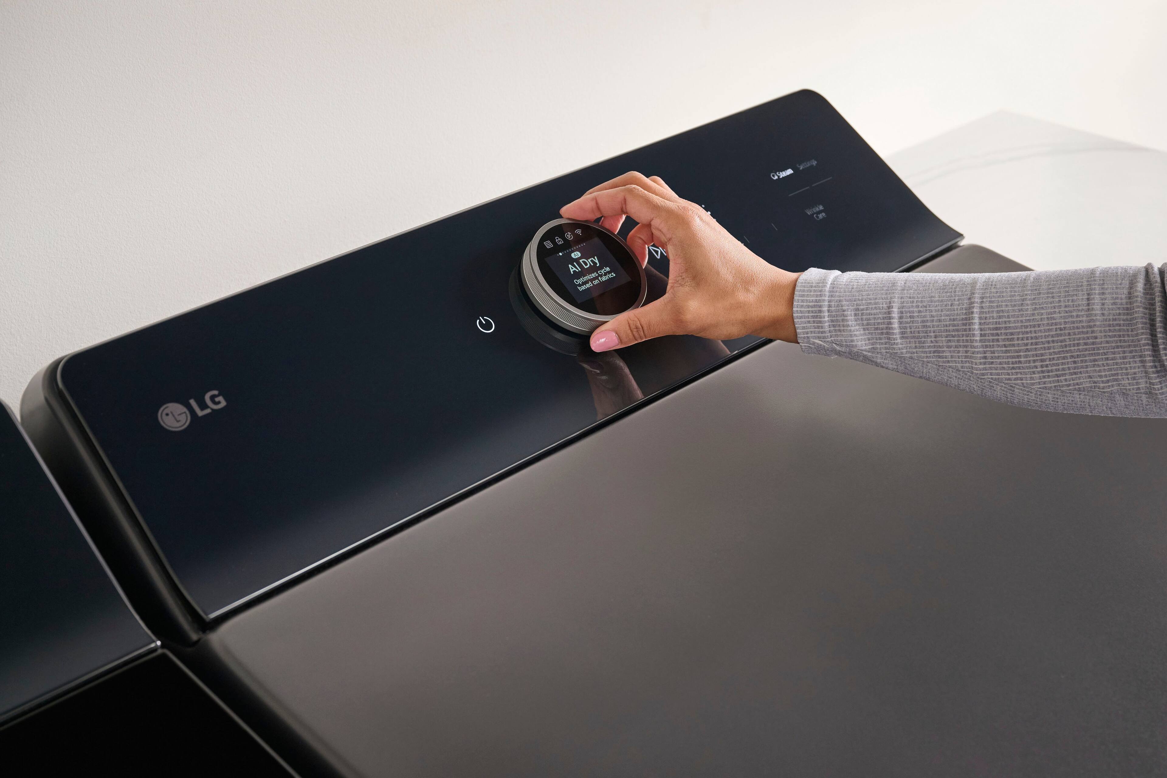 The image shows a person using a device, likely a smartphone, to check the time. The device is placed on top of a black object, which could be a table or a machine. The person's hand is on the device, and they are pressing a button or touching the screen to access the time. The image also features a clock, which is placed on the wall or another surface in the background.