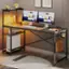 The image shows a desk with a computer setup, including a monitor, keyboard, and mouse. There is also a clock on the desk. Above the desk, there are two pictures hanging on the wall. The desk is located in a room with a rug on the floor. Additionally, there is a book and a handbag placed nearby.