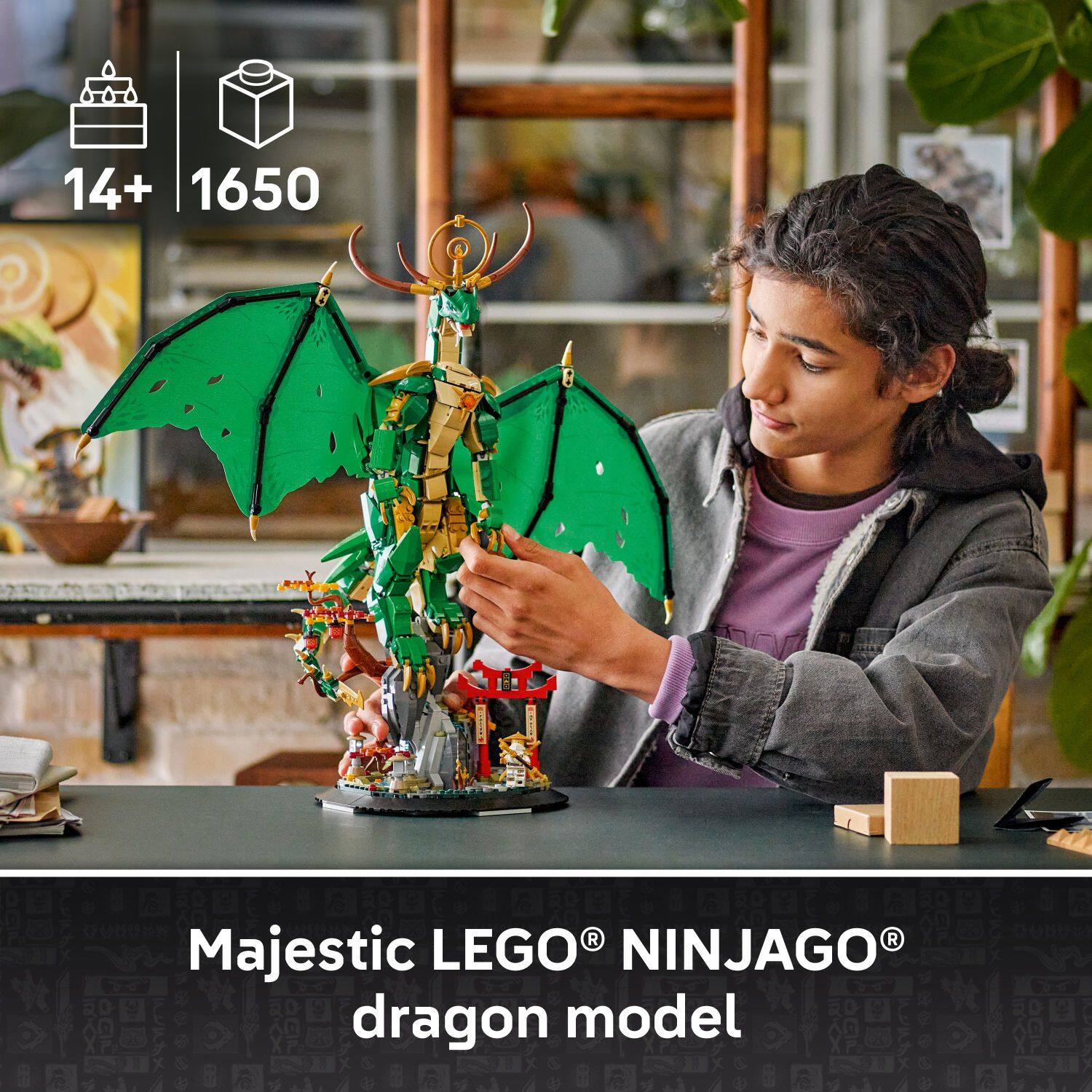 The image shows a person assembling a Majestic LEGO NINJAGO dragon model. The person is holding the model and working on it at a table. The model is quite large, with the dragon taking up a significant portion of the table. The person appears to be focused on putting the model together, likely enjoying the process of creating a unique and impressive display.