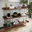 The image shows a wooden shelf with various items on it. The shelf has a collection of books, including a Vogue magazine, and a few vases. There are also two potted plants, one on the left side and another on the right side of the shelf. The shelf is placed on a wooden floor, and there are two vases on the shelf, one near the left side and another near the right side.