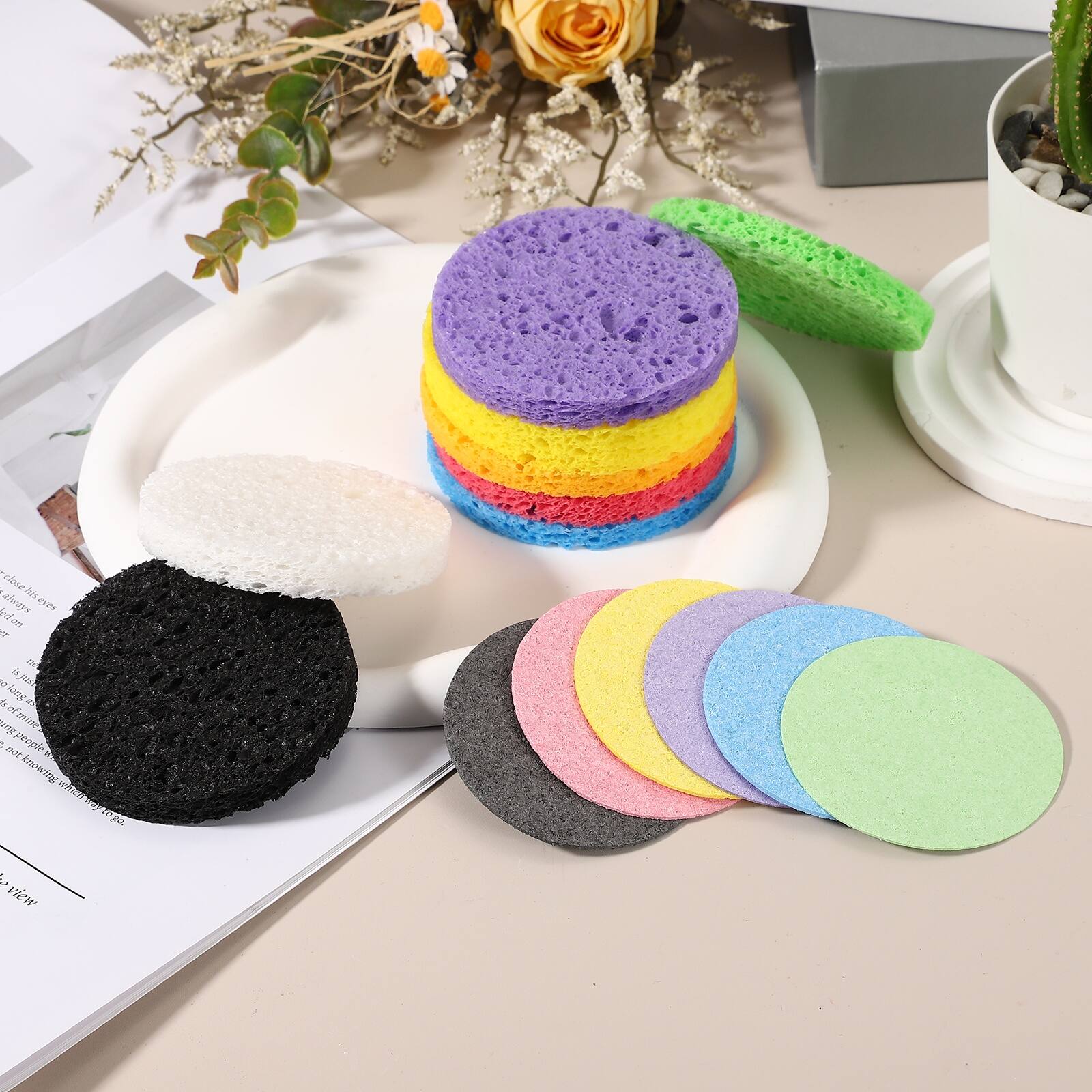 A close-up of a colorful sponge set on a white plate, with various sponges in different colors and textures, including black, white, green, purple, yellow, red, blue, and pink.
