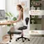 The image features a woman sitting on a chair in front of a computer desk. The chair is described as having a weight capacity of 385 lbs, and it is recommended for individuals who are between 5-6.3 feet tall. The woman is using a laptop, which is placed on the desk in front of her. The scene also includes a potted plant and a TV, both located near the woman.