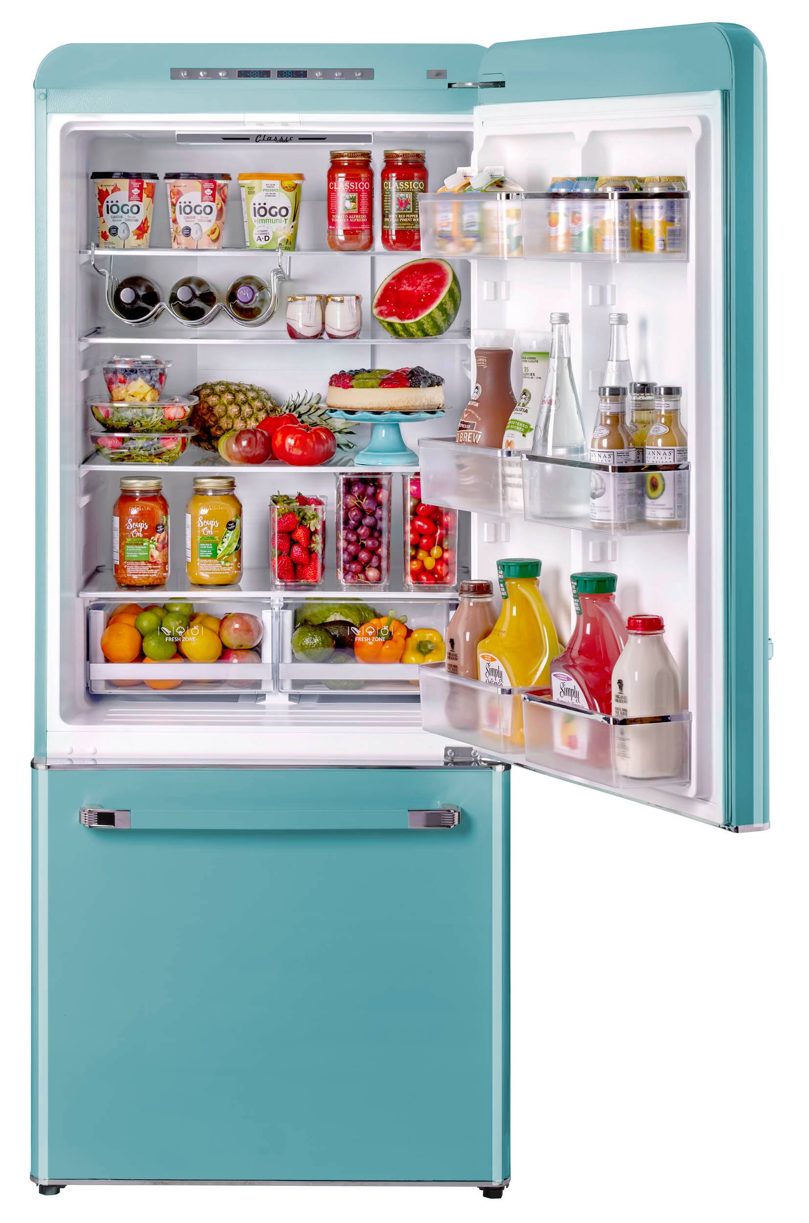 The refrigerator is filled with a variety of food items, including fruits, vegetables, and drinks. There are several bottles, some of which are placed in the door shelves, while others are placed in the main compartment. The refrigerator also contains a bowl and a cup, as well as a few apples and oranges. The assortment of food items and drinks makes the refrigerator appear well-stocked and ready for use.