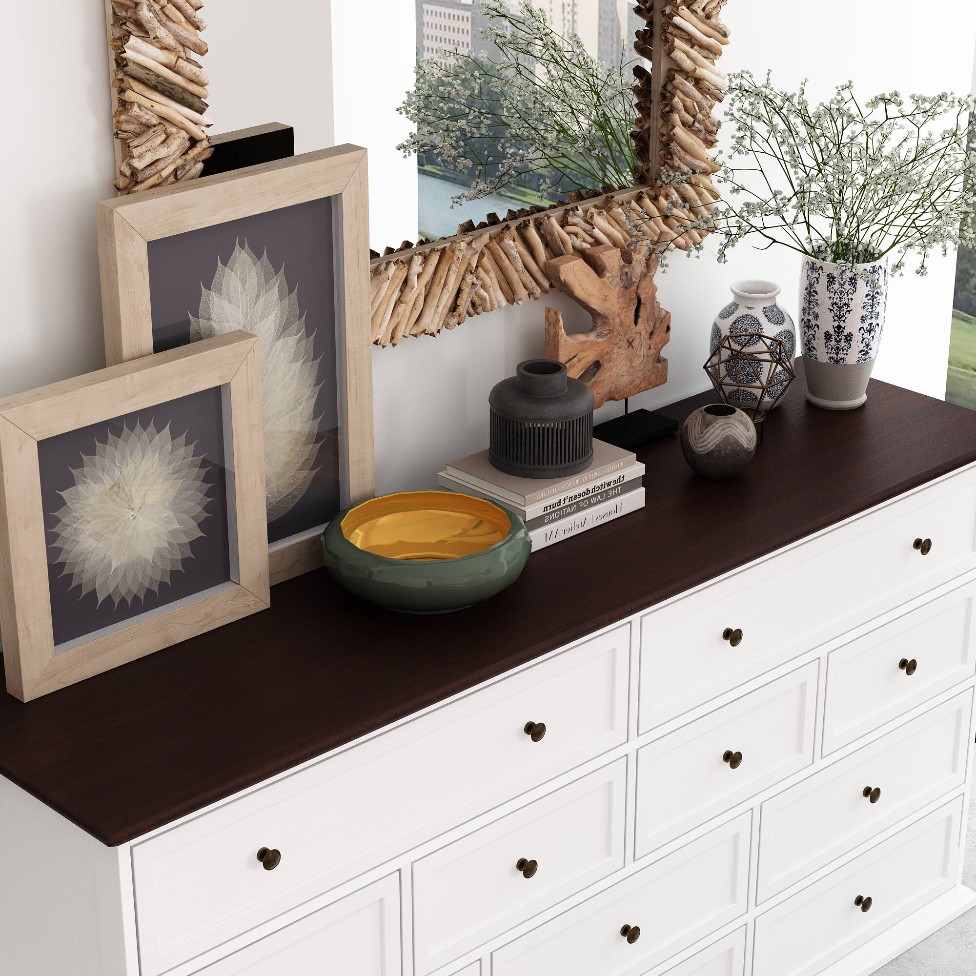 The image features a white dresser with a mirror above it. On the dresser, there are two pictures, a bowl, a vase, and a book. The bowl is placed in the middle of the dresser, while the vase is located towards the right side. The book is positioned towards the left side of the dresser. The dresser is adorned with a potted plant, which is placed on the left side of the dresser. The overall scene creates a cozy and organized living space.