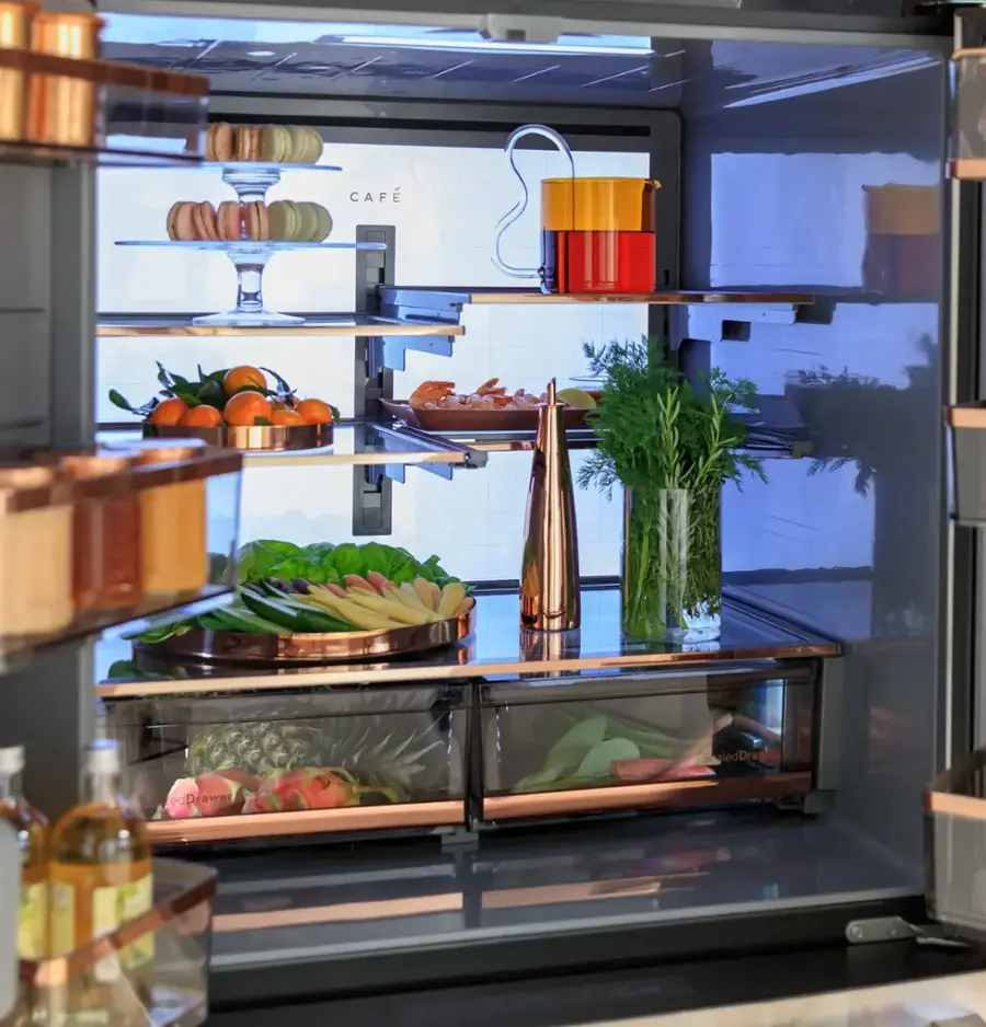 The image shows a refrigerator with its door open, revealing a variety of food items inside. The refrigerator is filled with fresh fruits and vegetables, including oranges, bananas, and broccoli. There are also several bottles and a wine glass placed in the refrigerator. The refrigerator is well-stocked, providing a variety of options for meal preparation.