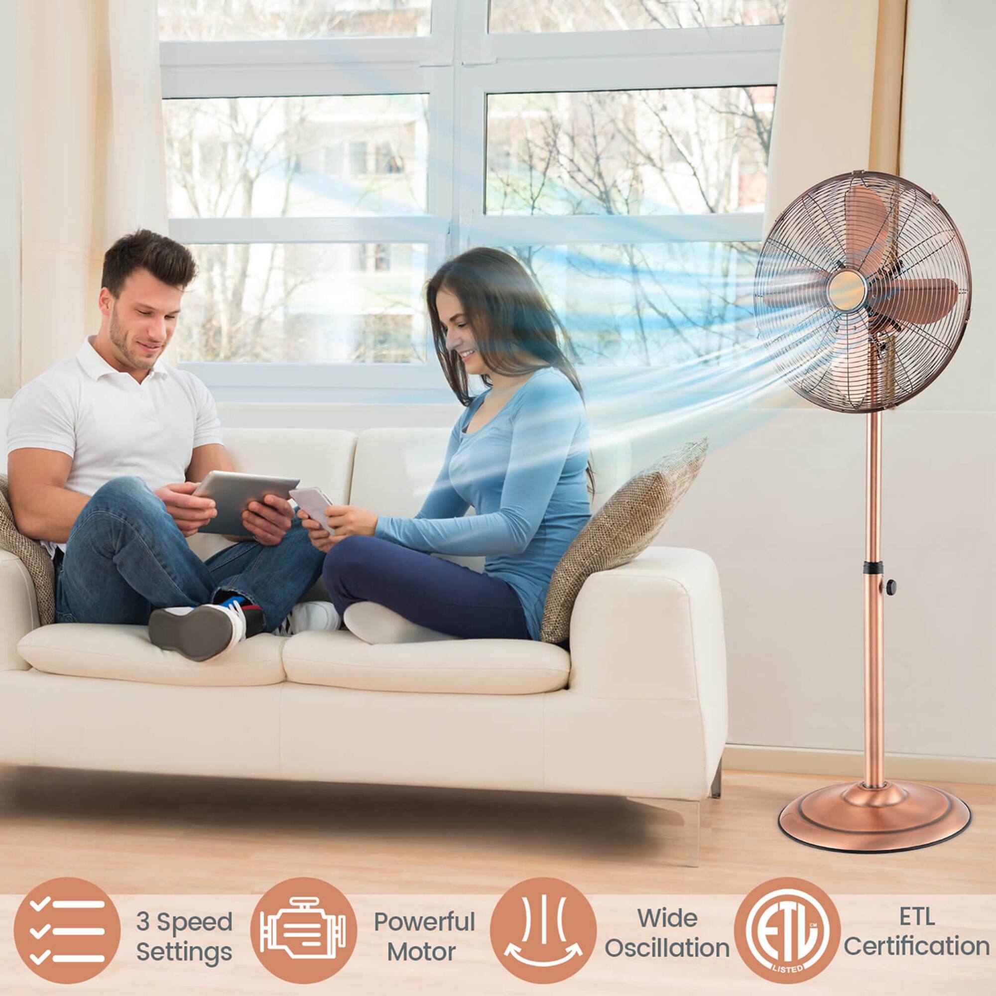 The image features a man and a woman sitting on a couch, each holding a tablet. They are both using the tablets, possibly for work or entertainment purposes. The scene is set in a living room, with a window nearby. There is a fan in the room, which might be used to create a comfortable environment. The woman is wearing a blue shirt, and the man is wearing a white shirt. The image also includes a bed, indicating that the living space is combined with a bedroom.