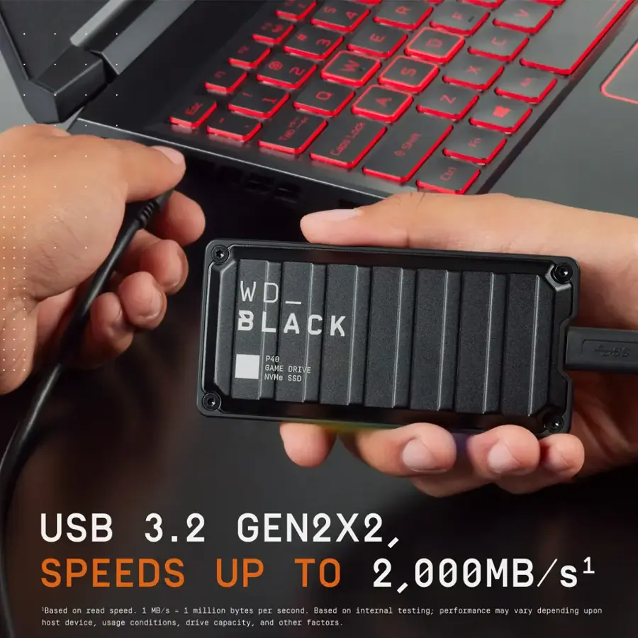 The text on the image reads:

"Esc E ! - ~ S 4 O > F I E I # m E O U ~ S X  1 O A ~ " f Lock Tab Shift Fn Ctrl WD_ BLACK P40 BAME DRIVE NVMe SSD 2ss USB 3.2 GEN2X2, SPEEDS UP TO 2,000MB/s1 Based on read speed. 1 MB/s . 1 million bytes per second. Based on internal testing; performance may vary depending upon host device, usage conditions, drive capacity, and other factors."

The text is about a WD Black P40 NVMe SSD, which is a high-speed storage device with read speeds of up to 2,000 MB/s. The text also mentions the use of a laptop and a thumb drive.