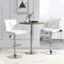 The image features a modern living room with two white chairs and a round table. The chairs are positioned on either side of the table, and there is a potted plant nearby. The room also contains a bookshelf with several books on display. The overall design of the space is minimalist and contemporary.