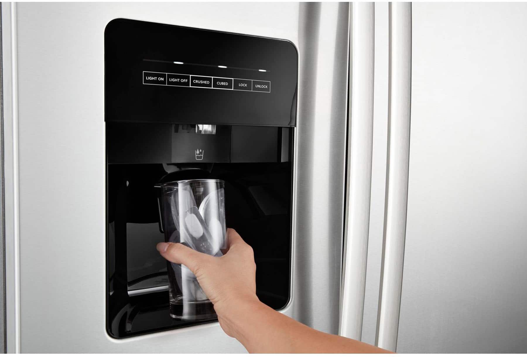 The image shows a person opening a refrigerator door with a glass of water inside. The refrigerator has a water dispenser with buttons for light on, light off, crushed ice, cubed ice, lock, and unlock. The person is pressing the button for crushed ice, which is located on the left side of the dispenser.