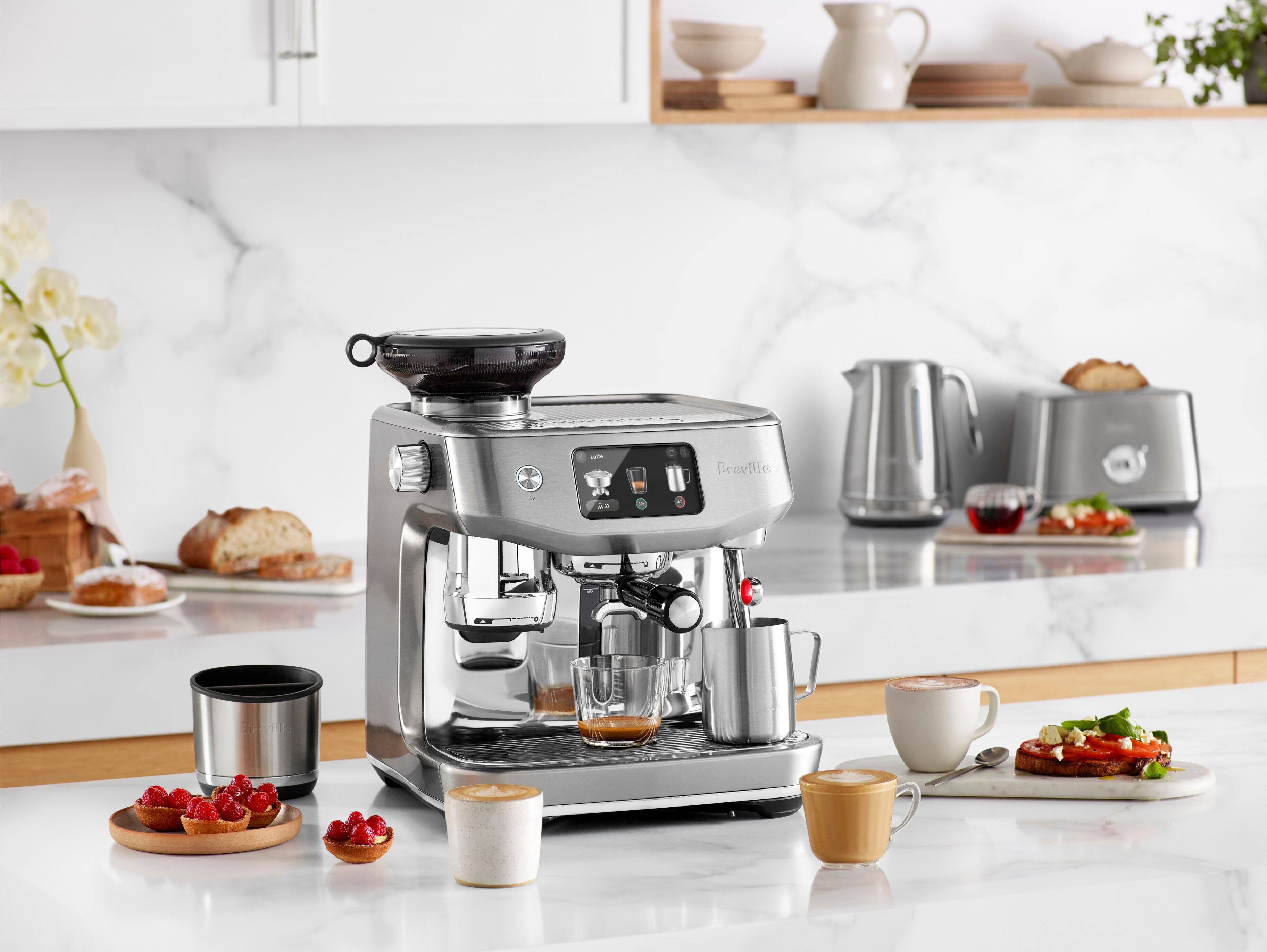 The image features a kitchen with a countertop that has a coffee maker, a toaster, and a blender on it. There are also various cups, bowls, and a vase placed around the kitchen. Additionally, there are several pieces of bread and a cake on the countertop. The kitchen is well-equipped with appliances and utensils, making it a functional space for preparing and enjoying meals.