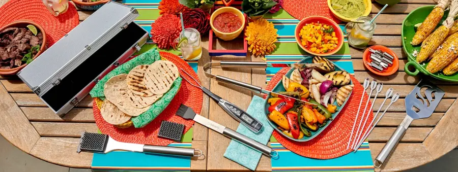 The image features a table filled with various foods and utensils. There are plates of food, including a plate of corn on the cob, and a bowl of food. The table also has a variety of utensils, such as forks, knives, and spoons, as well as a spatula. Additionally, there are several bowls placed on the table, containing different food items. The table is set up for a meal, with a variety of dishes and utensils to enjoy the food.