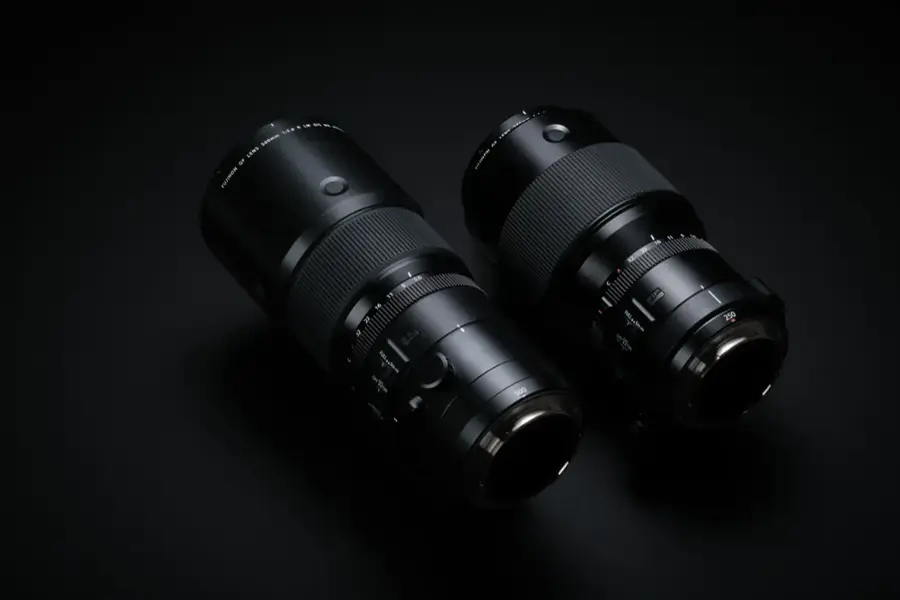The image features two camera lenses, which are placed next to each other on a black background. The lenses are large and black, and they are positioned in a way that they appear to be looking at each other. The lenses are likely designed for professional photography or videography, as they are of high quality and have a significant focal length.