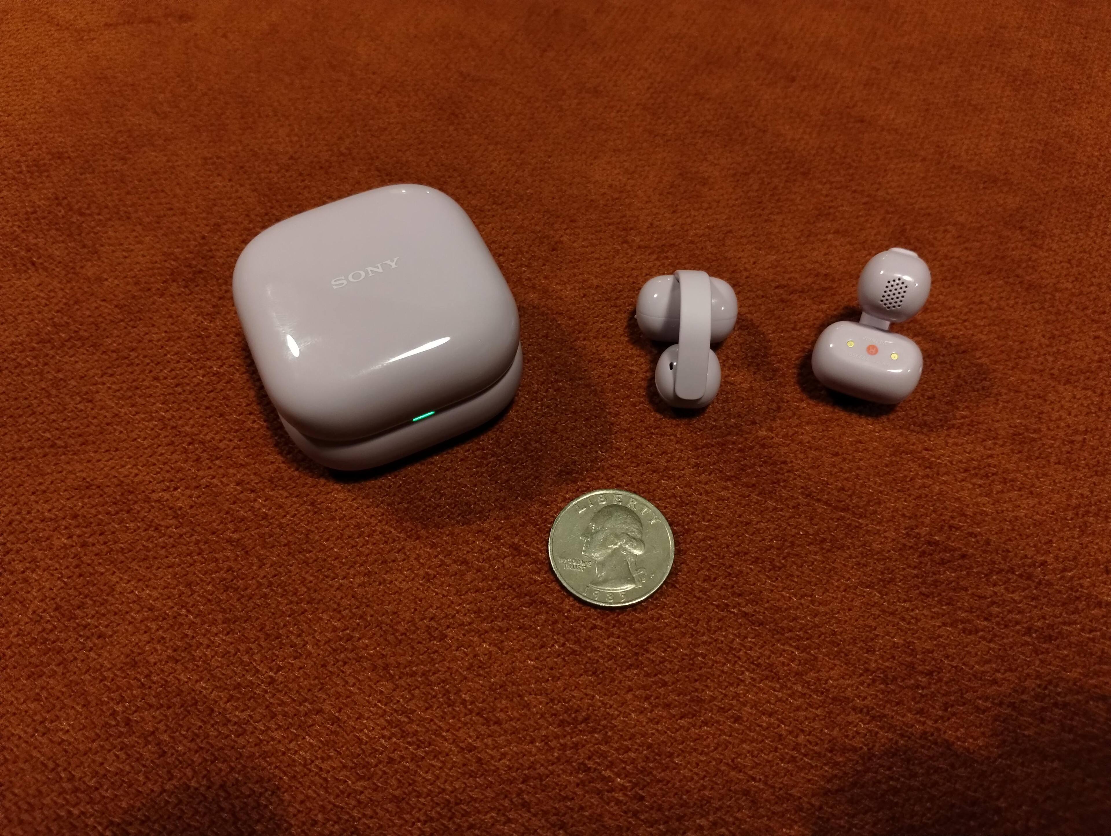 Case Closed, and you can see the case LED lit green.  Left and right ear bud, you can see the red circle with the "R" for "Right" on the Right ear bud.  The left has a white circle with an "L" in it.  There is a quarter there to give an idea of the size., click to load a larger version